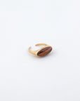 The For Art's Sake® Enza Ring, made from gold-plated stainless steel, showcases an oval-shaped brown gemstone set against a plain white background. Its open back and polished enamel finish complement its elegant and minimalist design.