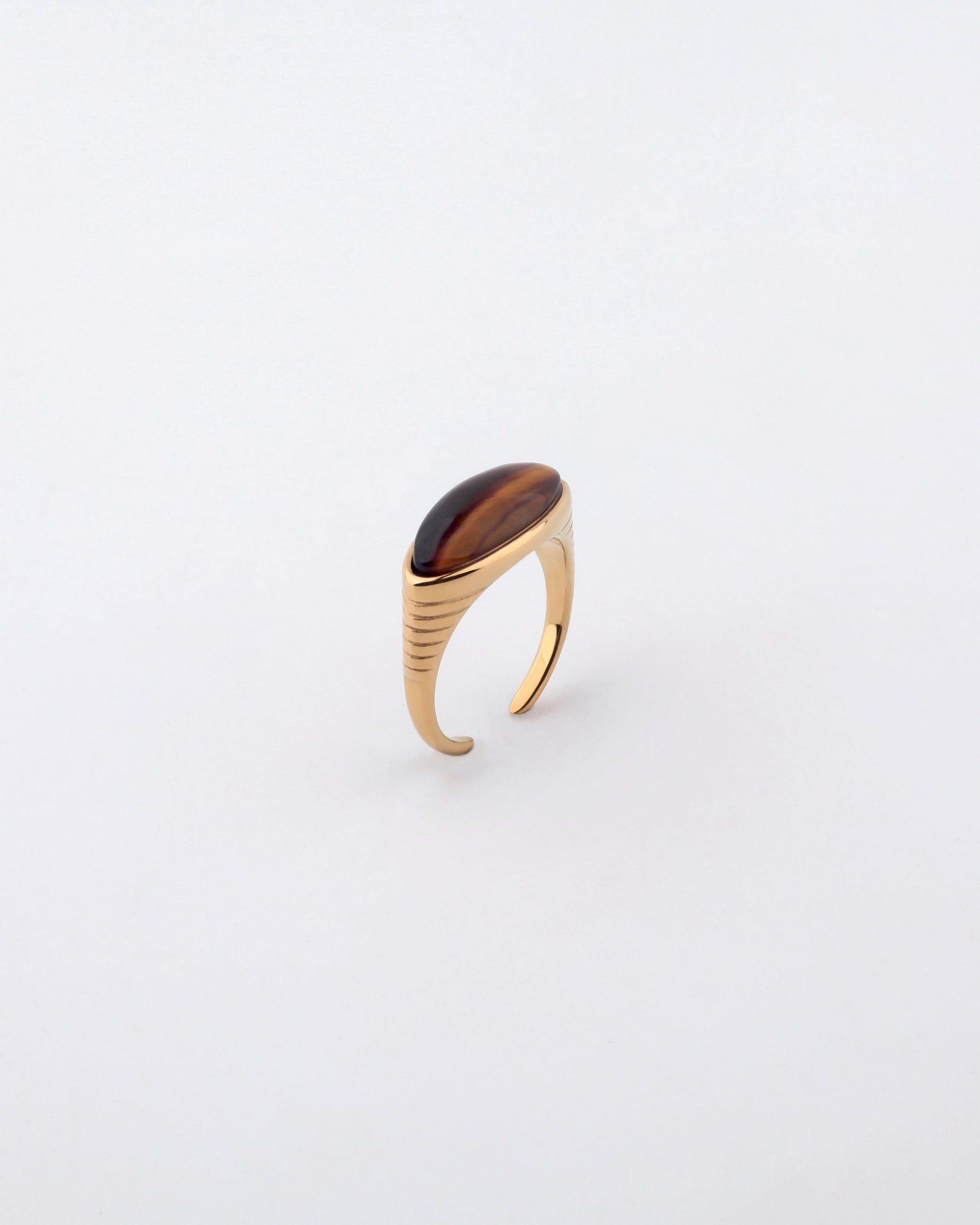 A gold-plated stainless steel Enza Ring by For Art's Sake® with a large oval-shaped brown gemstone sits against a plain white background. The ring features a minimalist design, with subtle grooves along the band leading up to the polished enamel finish of the stunning stone.