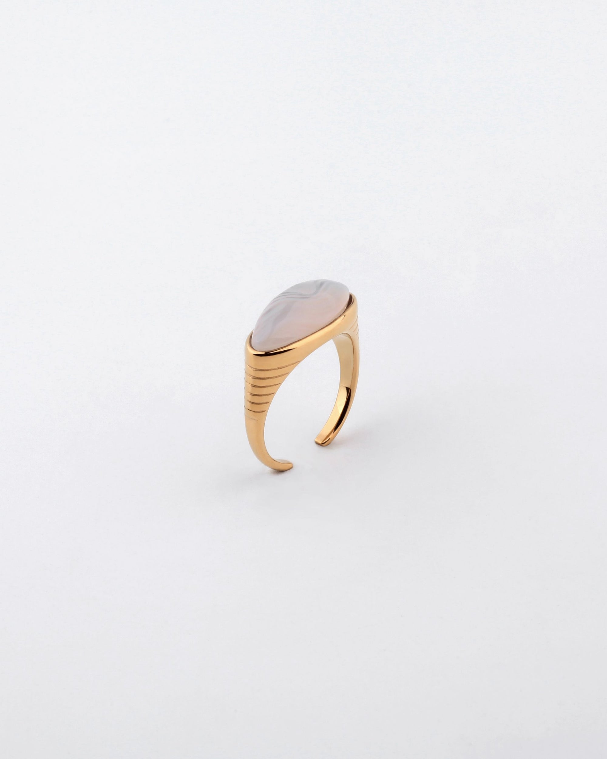 A gold-plated stainless steel ring from For Art's Sake®, featuring a smooth, oval inset stone, is photographed against a white background. The Enza Ring's band is adorned with subtle horizontal lines near the setting, giving it a contemporary and elegant design.