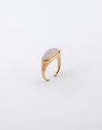 A gold-plated stainless steel ring from For Art's Sake®, featuring a smooth, oval inset stone, is photographed against a white background. The Enza Ring's band is adorned with subtle horizontal lines near the setting, giving it a contemporary and elegant design.