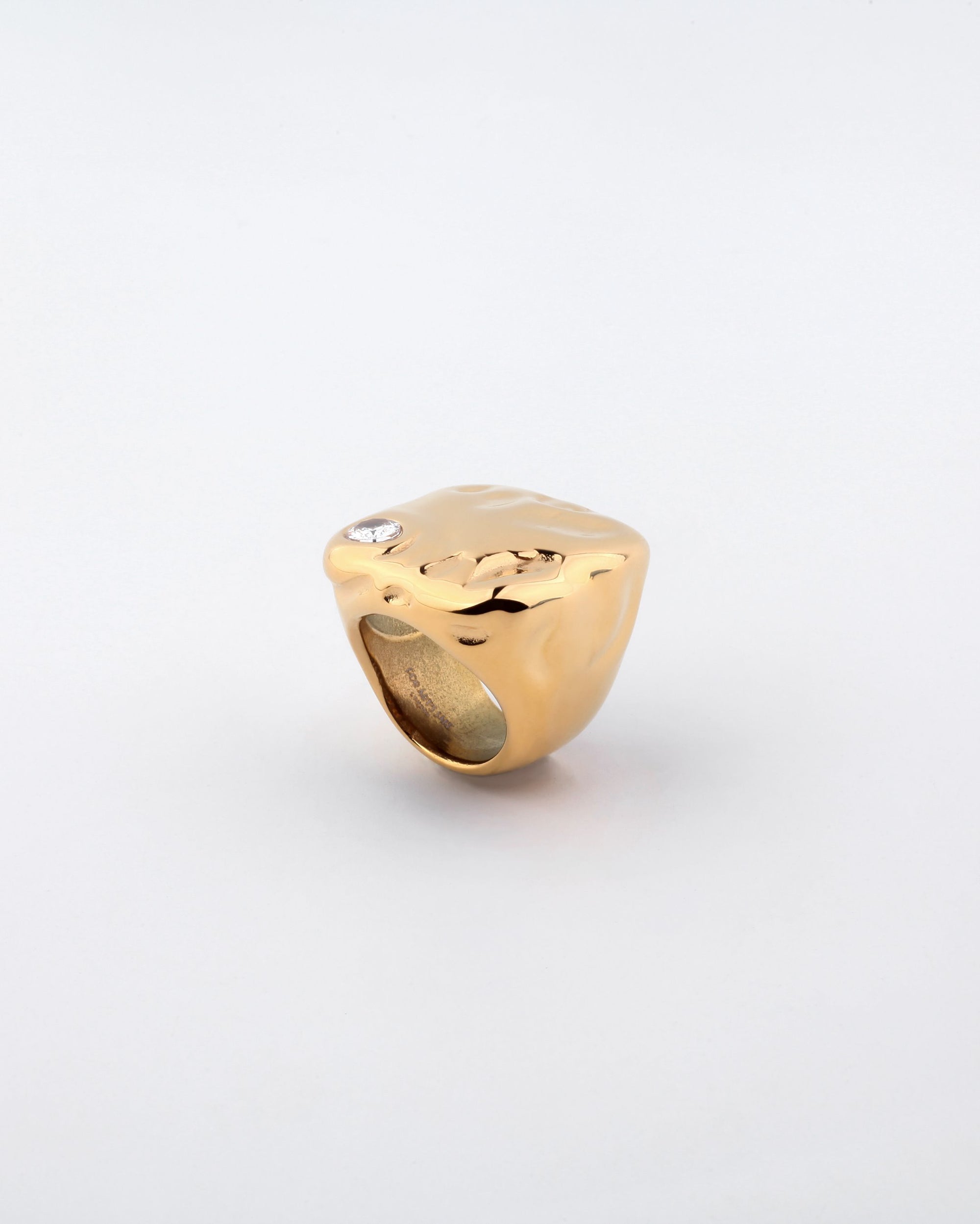 A Chiara Ring by For Art&#39;s Sake®, featuring a polished gold signet design with a broad, smooth surface and a single small crystal embellishment set near one corner, against a plain white background.