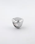 Introducing the Chiara Ring by For Art's Sake®: a polished, silver-plated masterpiece. This ring boasts a thick, square-shaped band with smooth, rounded edges and features an eye-catching abstract wavy surface. A small, sparkling gemstone embedded near one corner adds a touch of elegance against its plain white backdrop.