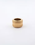 A gold Metallic Woven Ring by For Art's Sake® with an 18kt gold-plated, ribbed design is placed centrally against a white background. The ring features a cylindrical shape with a hollow center.