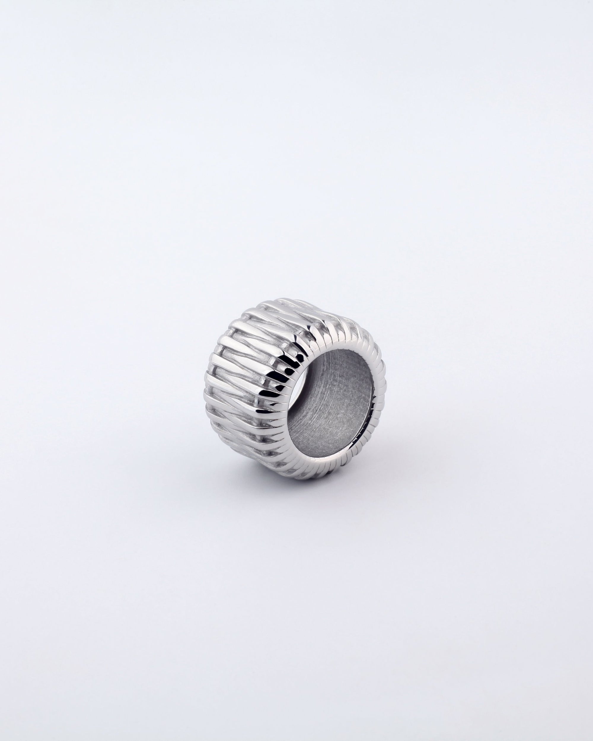 The Woven Ring by For Art&#39;s Sake® is a silver, 18kt gold-plated piece featuring a wide band with ribbed texture on its exterior. Displayed against a plain white background, the design boasts vertical grooves encircling the entire circumference.