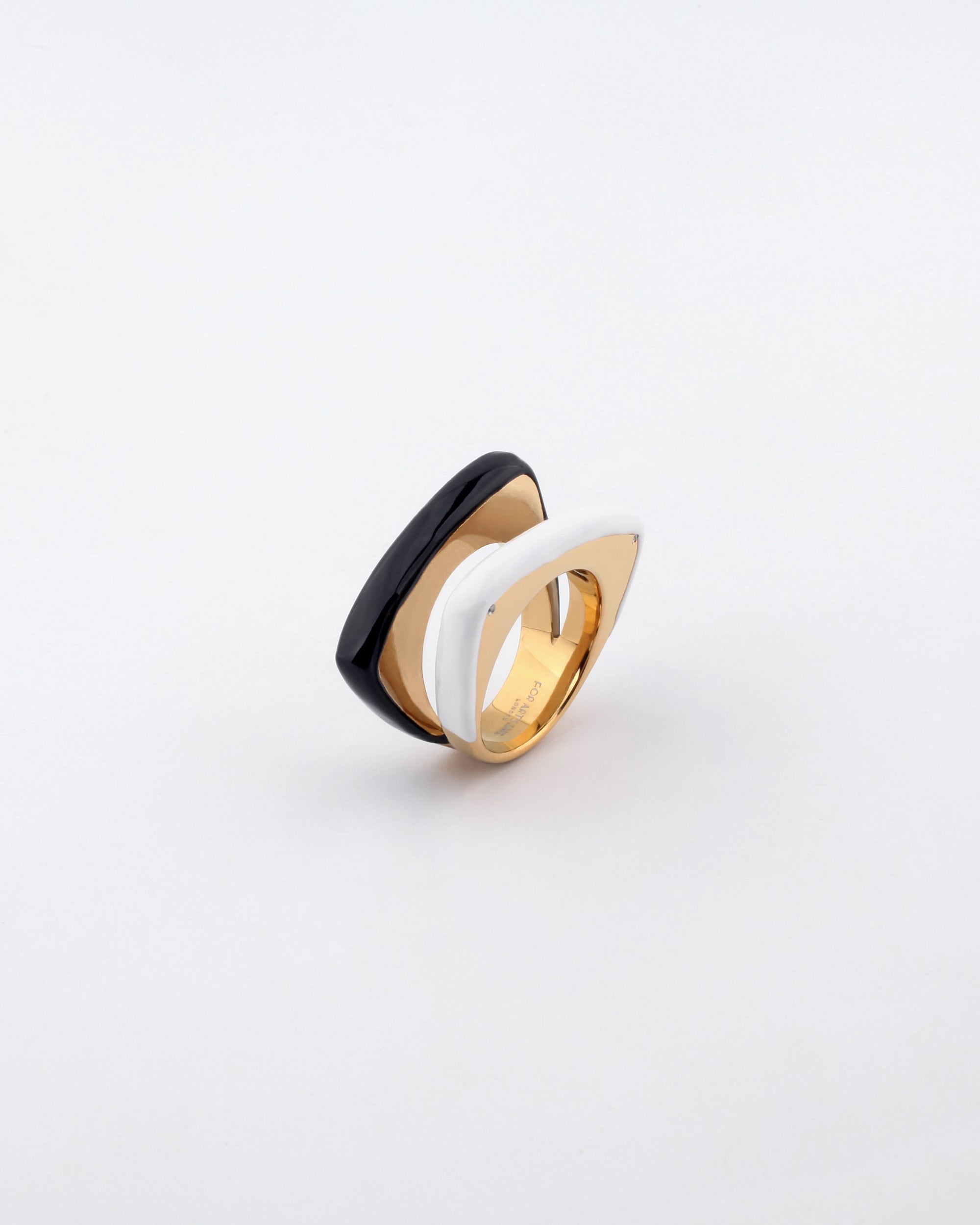 A stylish Delta Ring by For Art's Sake®, showcasing a distinctive layered design with a chic black and white contrasting color scheme. The ring exudes a modern aesthetic with its smooth, curvy shapes seamlessly blending into a polished gold base, beautifully set against a plain white backdrop.