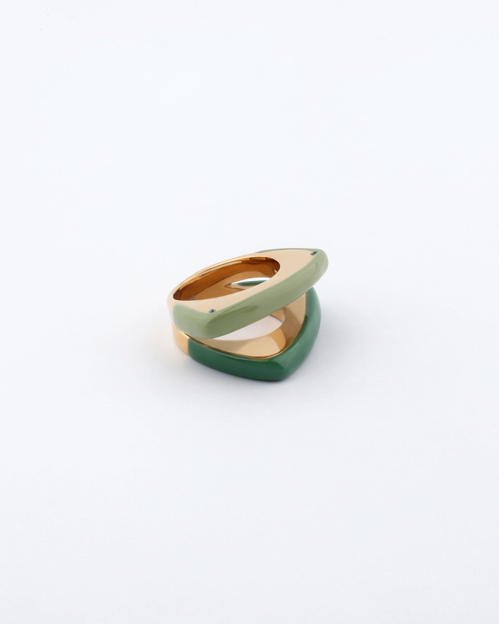 A photograph of the For Art's Sake® Delta Ring, showcasing two overlapping geometric rings. The upper ring features a pale green color and a smooth surface, while the lower ring boasts a bold splash of deep green. Both rings display a unique layered design, rounded and modern against a plain white background.