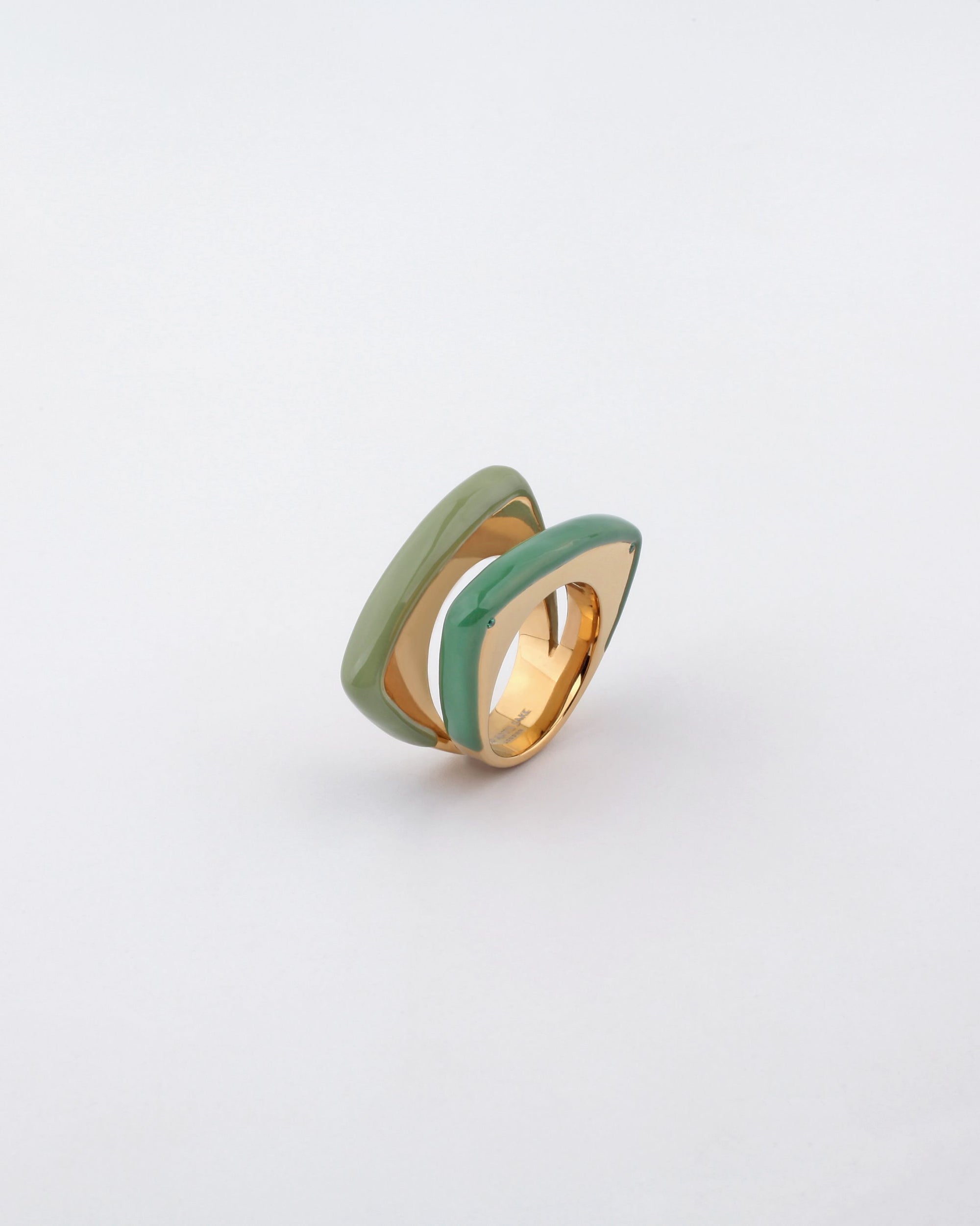 The Delta Ring by For Art's Sake® is a modern gold ring with a unique layered design, featuring two parallel sections of glossy enamel in light green and mint green. These sections create a sleek, curved effect on either side of the gold band, adding a bold splash of color against the plain white background.