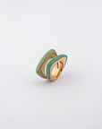 The Delta Ring by For Art's Sake® is a modern gold ring with a unique layered design, featuring two parallel sections of glossy enamel in light green and mint green. These sections create a sleek, curved effect on either side of the gold band, adding a bold splash of color against the plain white background.