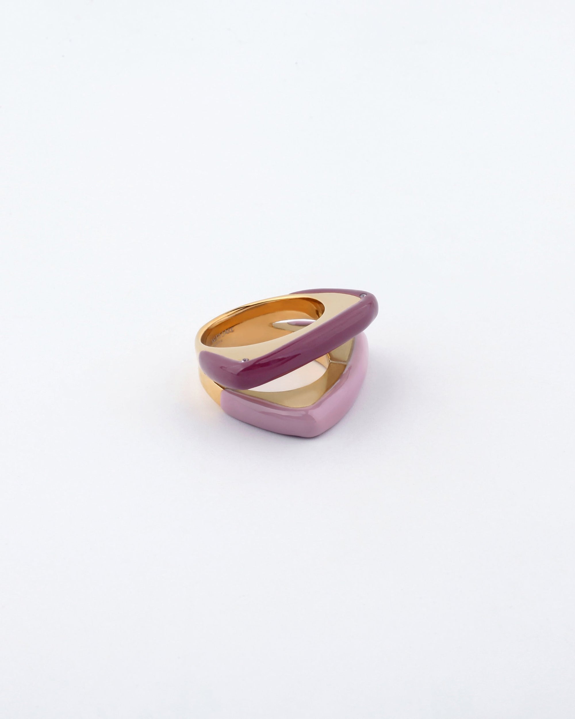 Introducing the For Art&#39;s Sake® Delta Ring, a modern accessory featuring intertwining bands of gold-tone metal and a glossy pink enamel finish, set against a plain white background. The layered design boasts contemporary aesthetics, making it perfect for lovers of minimalistic fashion.