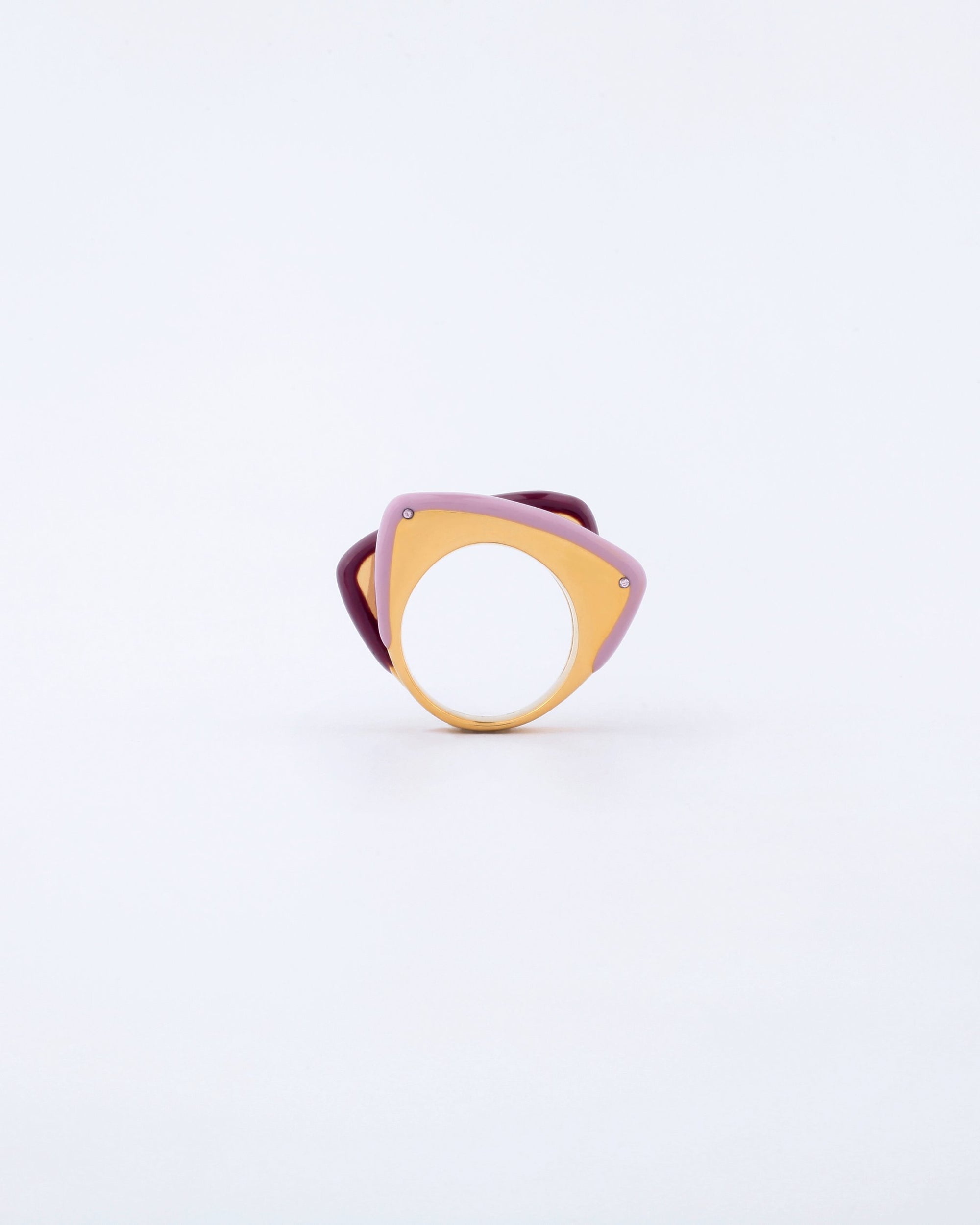 The Delta Ring by For Art's Sake® is a uniquely designed piece featuring a large circular hole in the center. Its abstract shape combines shades of purple and gold with a matte finish. The layered design appears modern and artistic, creating a striking visual contrast against the plain white background.