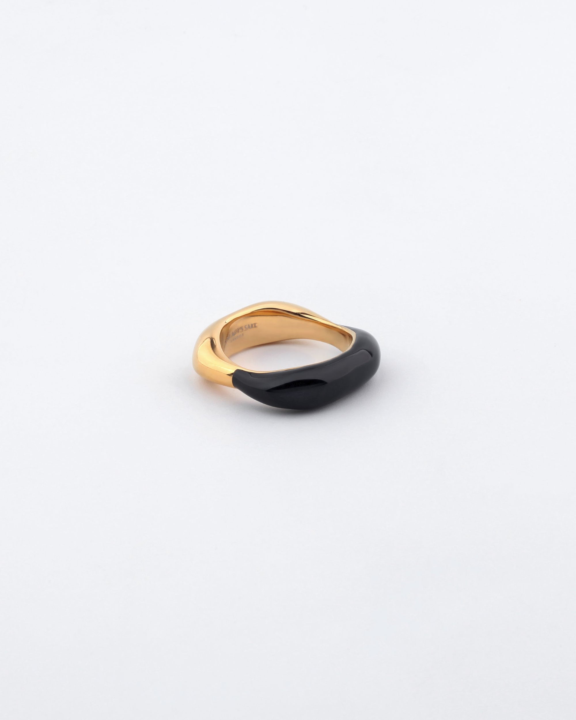 The Raya Ring by For Art&#39;s Sake® is a piece of contemporary jewelry that boasts a minimalist design with a band transitioning from polished gold to shiny black. Its smooth and flowing shape creates an elegant and modern look, set against a plain white background.