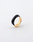 A Raya Ring from For Art's Sake® with a large, smooth black oval stone embedded in it is displayed on a white background. The inner band features an engraved inscription. This gold-toned metal ring has a modern, elegant design.