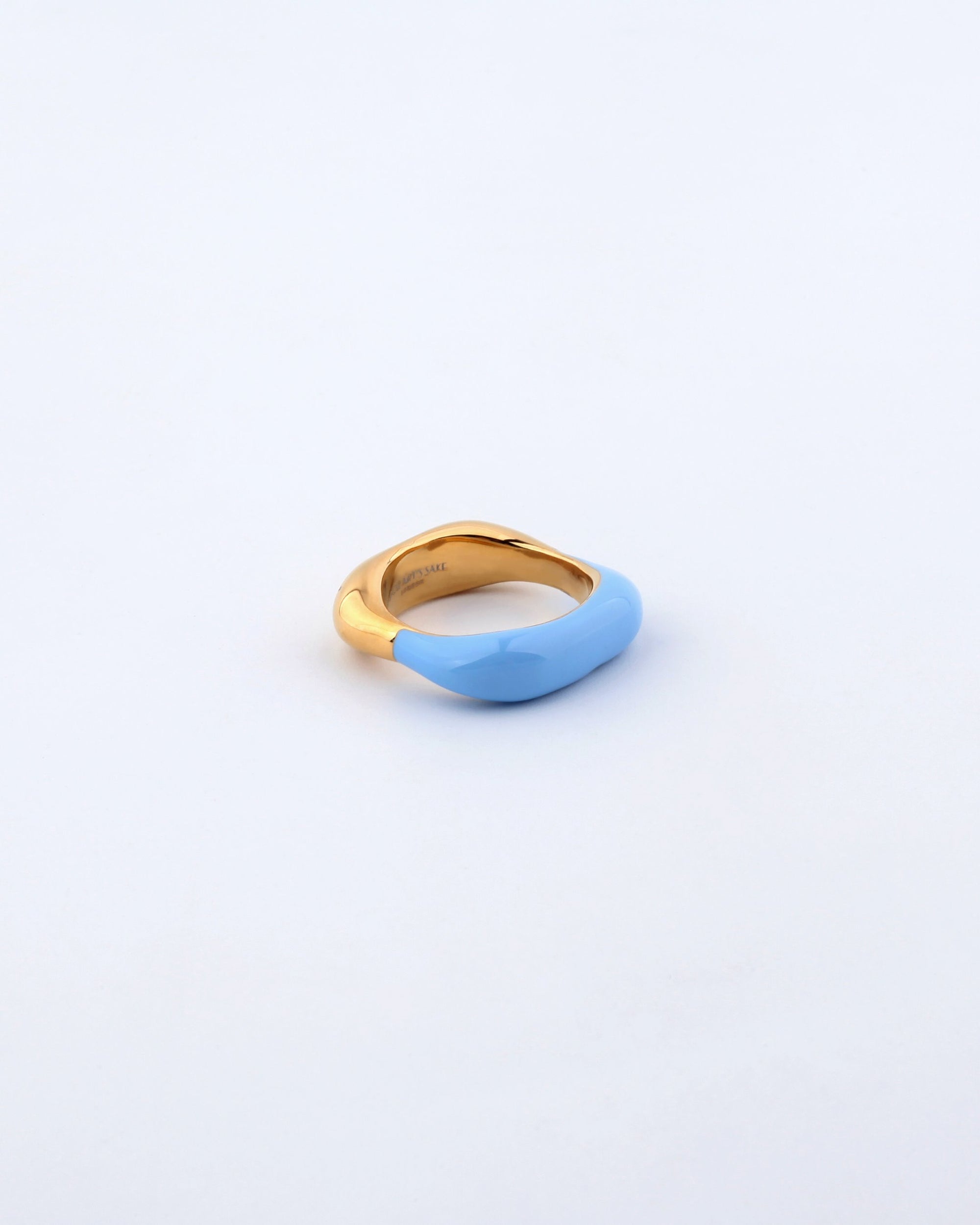 Introducing the Raya Ring by For Art&#39;s Sake®: a uniquely designed piece where one half is coated in smooth, light blue enamel. The gold-toned metal seamlessly blends with the blue, creating a visually stunning contrast. Set against a plain, light background, this colored enamel ring stands out beautifully.