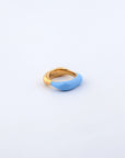 Introducing the Raya Ring by For Art's Sake®: a uniquely designed piece where one half is coated in smooth, light blue enamel. The gold-toned metal seamlessly blends with the blue, creating a visually stunning contrast. Set against a plain, light background, this colored enamel ring stands out beautifully.