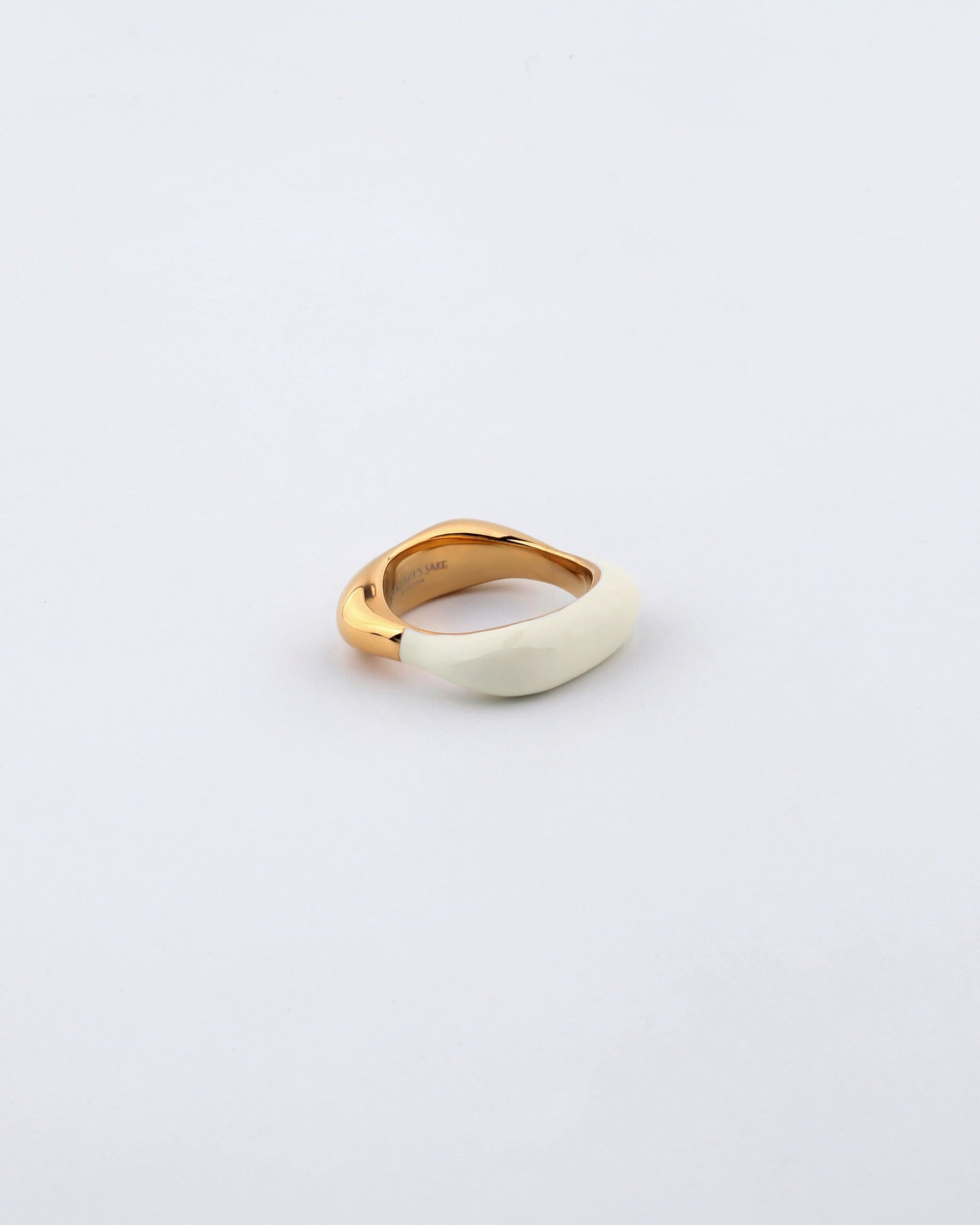 A close-up of the For Art&#39;s Sake® Raya Ring against a white background. This piece of contemporary jewelry features a minimalist design with a smooth, irregular shape; one half in polished gold and the other in an elegant cream or ivory finish.