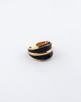 A stylish, open-ended Maven Ring by For Art's Sake®, featuring a sleek black band intertwined with shining gold-toned metal accents, displayed on a clean white background. The design is modern and elegant, making a bold statement.