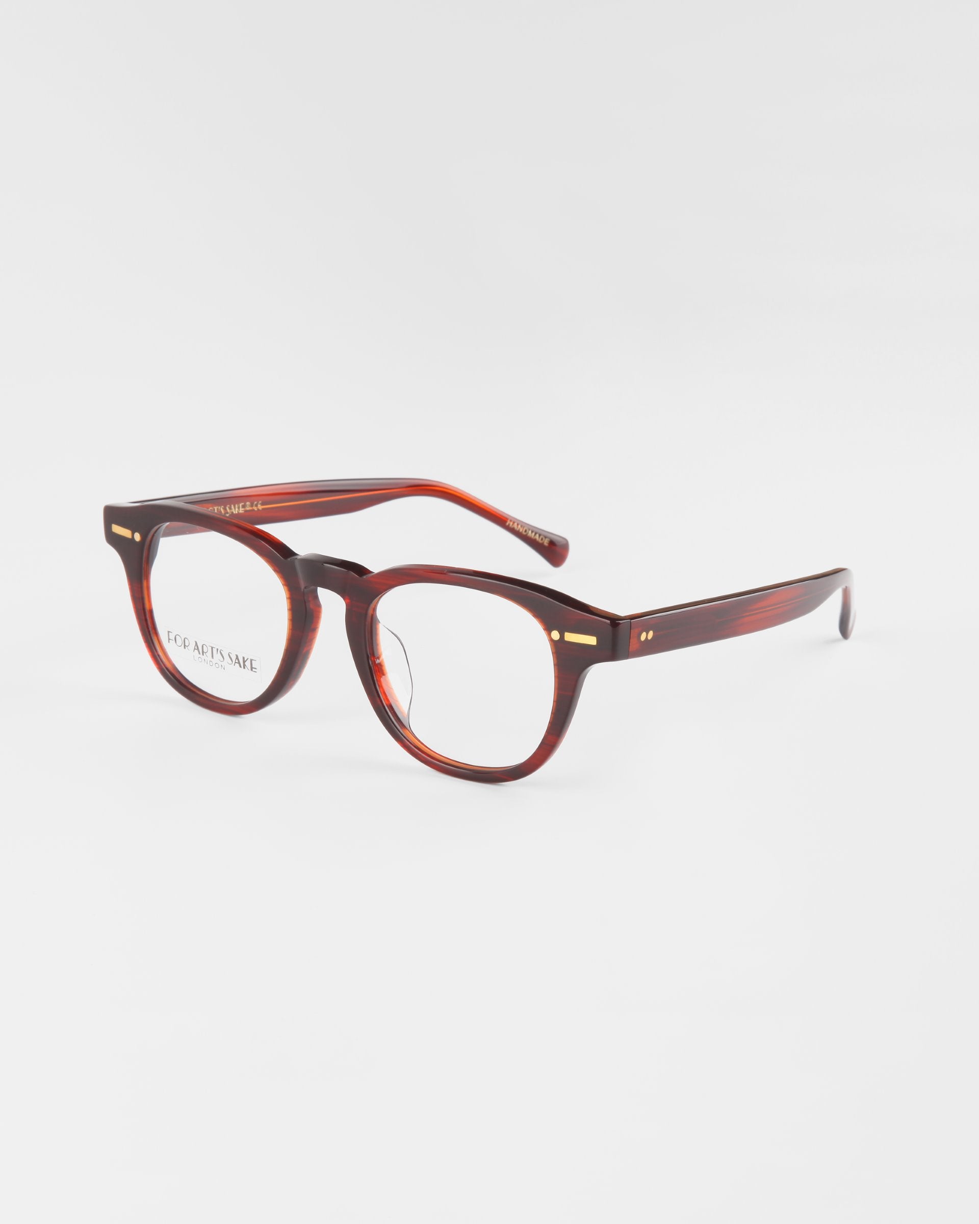 A pair of Rocky Brown eyeglasses by For Art's Sake® with round lenses and a sturdy bridge. The frames have gold accents near the hinges and a sleek, glossy finish. Featuring UV protection, the temple arms are thick and taper slightly towards the ear tips. Background is white.