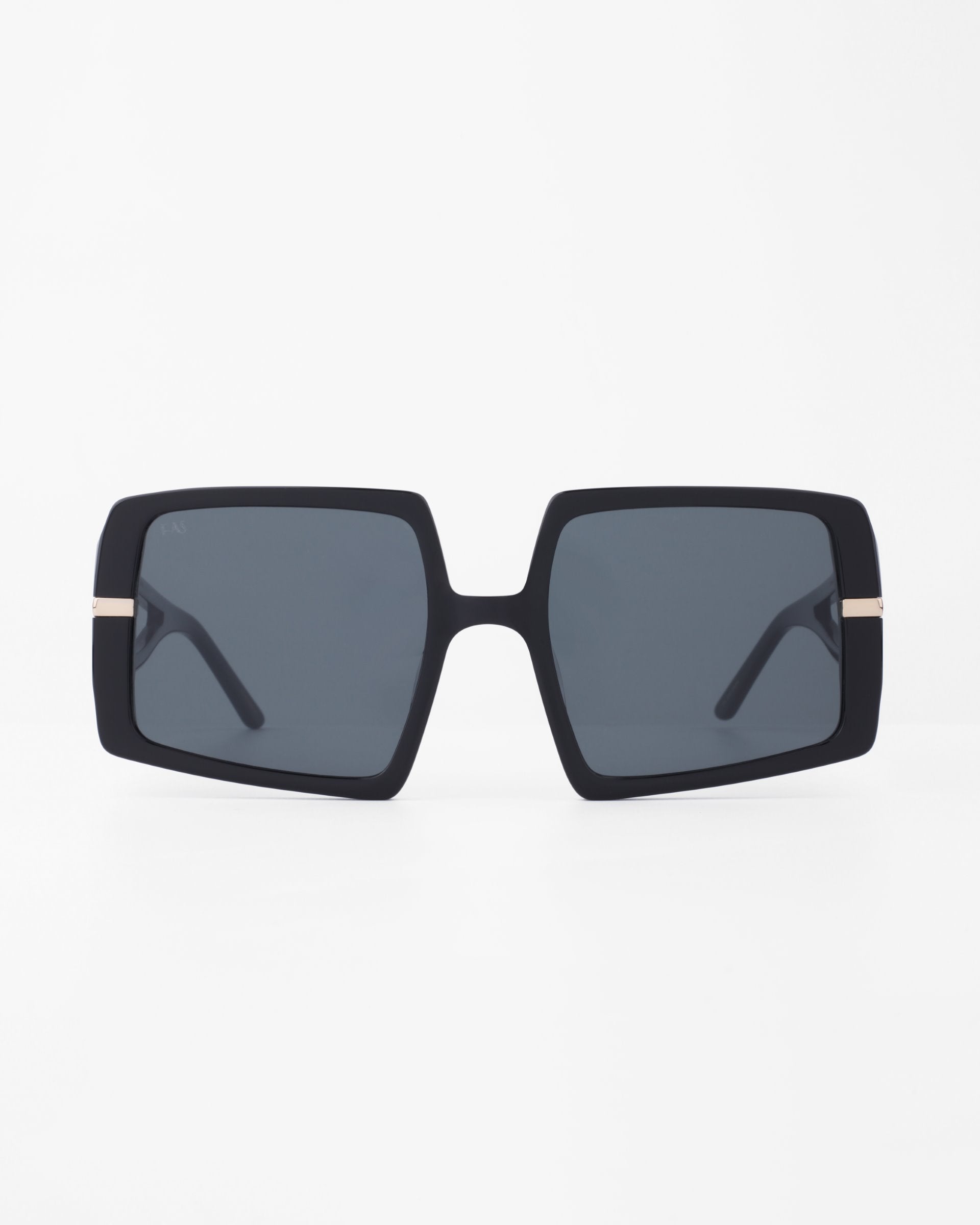 A pair of oversized, black-framed sunglasses with square, shatter-resistant nylon lenses. The darkly tinted lenses are complemented by a plant-based acetate frame featuring a small, 18-karat gold-plated accent on the temples near the hinges. The background is plain white. This is the Saturday by For Art&#39;s Sake®.