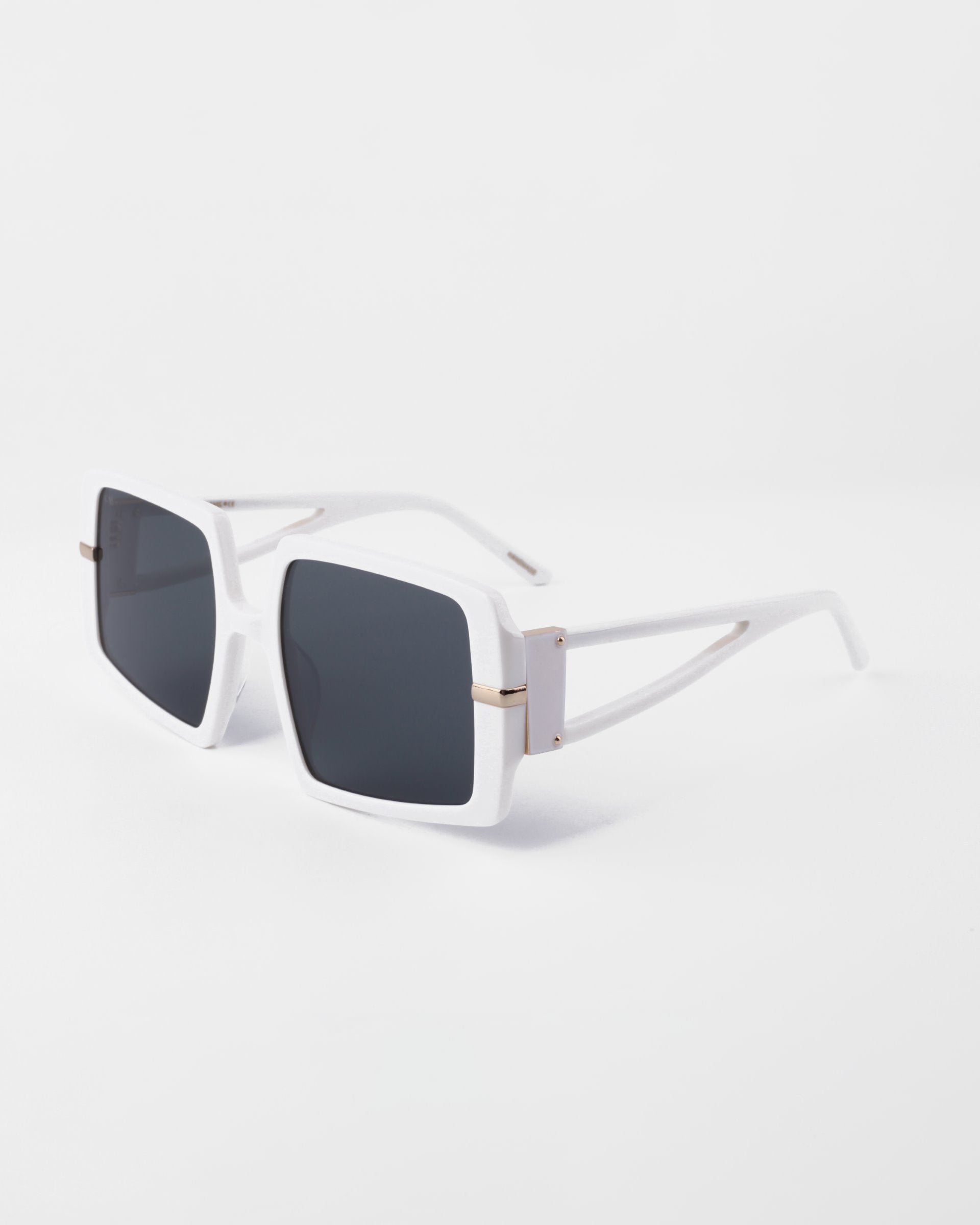 A pair of modern white-framed sunglasses with large, square, shatter-resistant nylon lenses. The white temples feature a cutout design near the hinges. Crafted from plant-based acetate, they offer both style and sustainability. These are the Saturday by For Art&#39;s Sake®. The background is a smooth, neutral white.