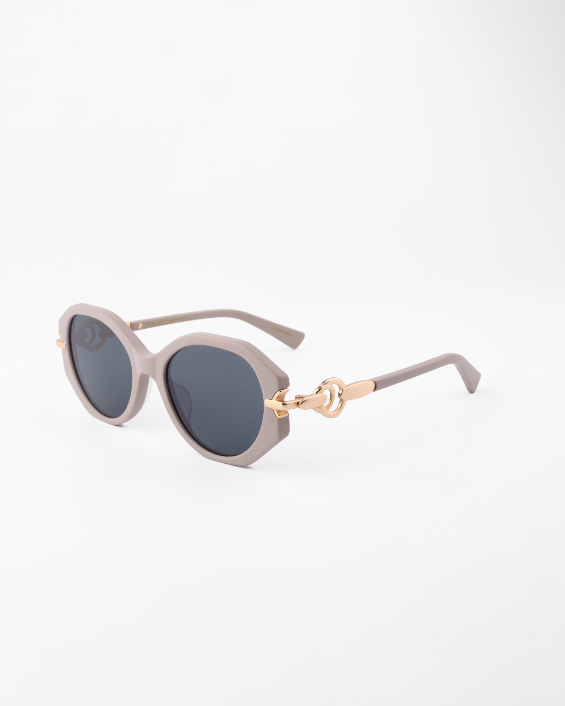 A pair of stylish Seaside, round sunglasses with dark, shatter-resistant lenses and light grey handmade acetate frames from For Art&#39;s Sake®. The arms feature a decorative gold-colored accent near the hinges. They are placed on a plain white surface.