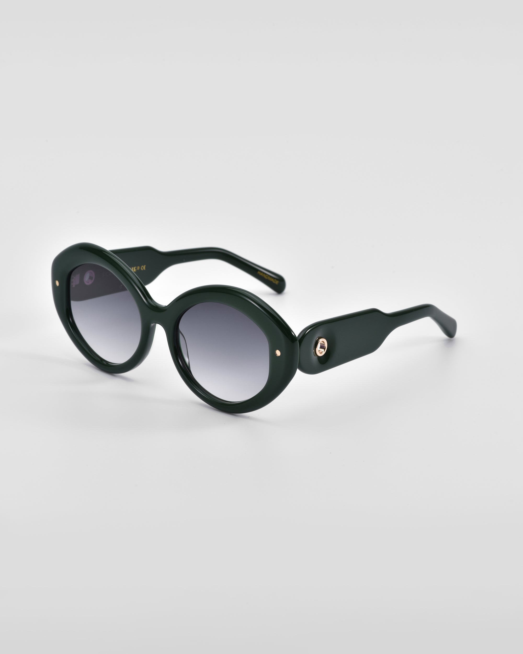 A pair of dark green, oval-shaped Helios sunglasses from For Art&#39;s Sake® with thick frames and gradient lenses. The arms, also thick, feature a small, circular metallic accent near the hinges. This piece of luxury eyewear stands out against the plain white background.
