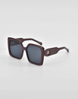 A pair of stylish, oversized, square-framed For Art's Sake® Eos sunglasses with dark lenses and thick, dark brown frames. The sunglasses are positioned against a plain white background, showcasing their design details clearly.