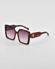 A pair of oversized soft-square sunglasses with brown tortoiseshell frames and gradient lenses. The thick frames feature classic temple round details and wide arms that taper as they extend. The **Eos** sunglasses by **For Art's Sake®** are positioned on a plain white background.