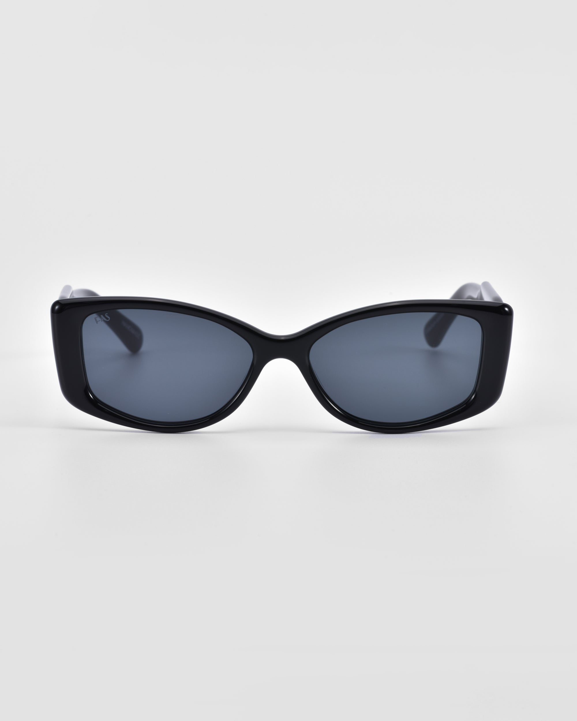 A pair of stylish black Mene sunglasses from For Art&#39;s Sake® with dark lenses is centered against a plain white background. The frame, featuring luxury frames with a sleek and slightly curved design, gives it a modern look. The sunglasses boast a simple yet fashionable style.