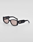 A pair of black rectangular Mene sunglasses with pink-tinted lenses from For Art's Sake® is displayed against a plain white background. The luxury frames have thick edges and feature a small, round embellishment near the hinges on each side.