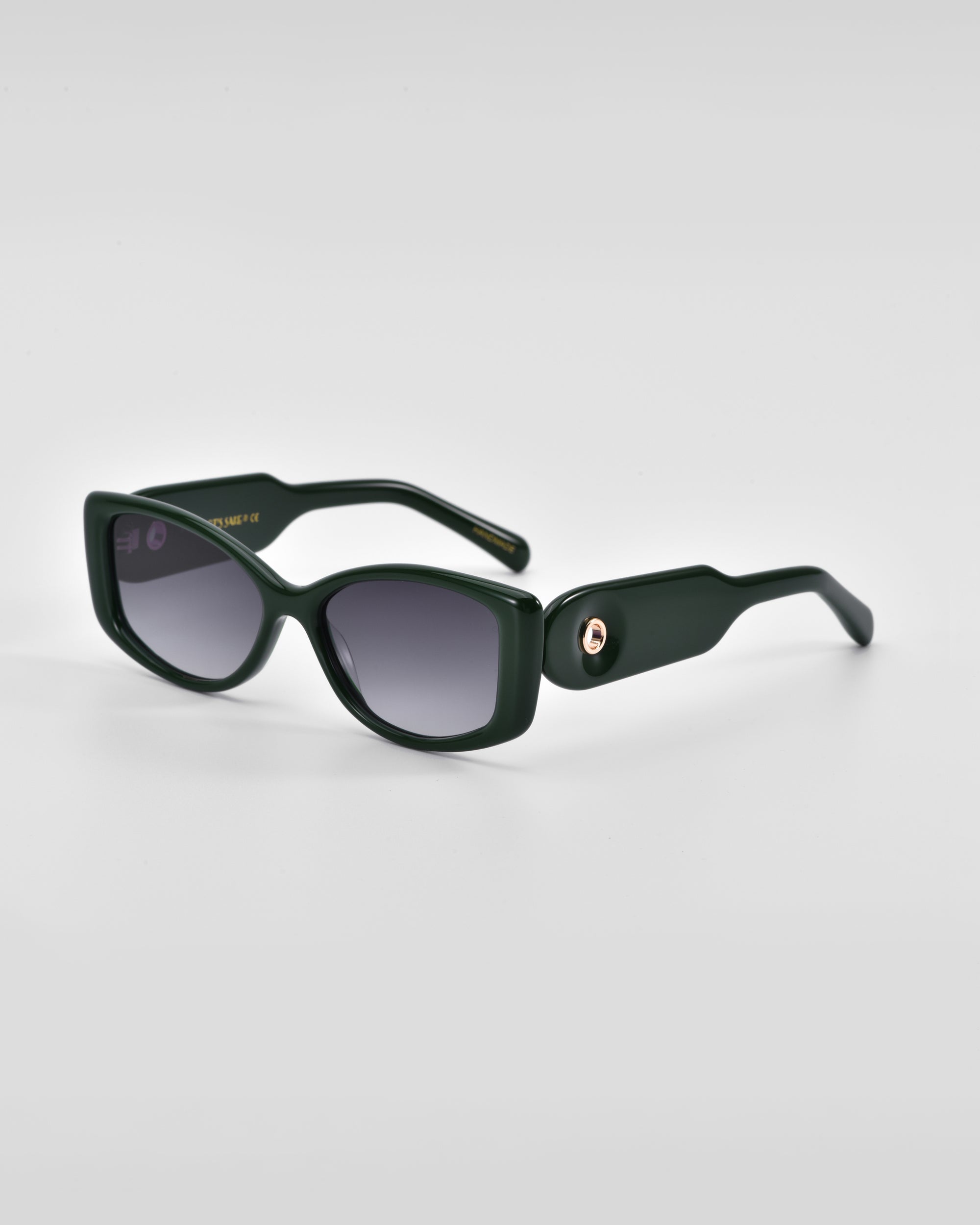 A pair of stylish, dark green For Art&#39;s Sake® Mene sunglasses with rectangular frames and dark tinted lenses. The left temple arm features a luxurious 18 karat gold accent near the hinge on a plain white background.