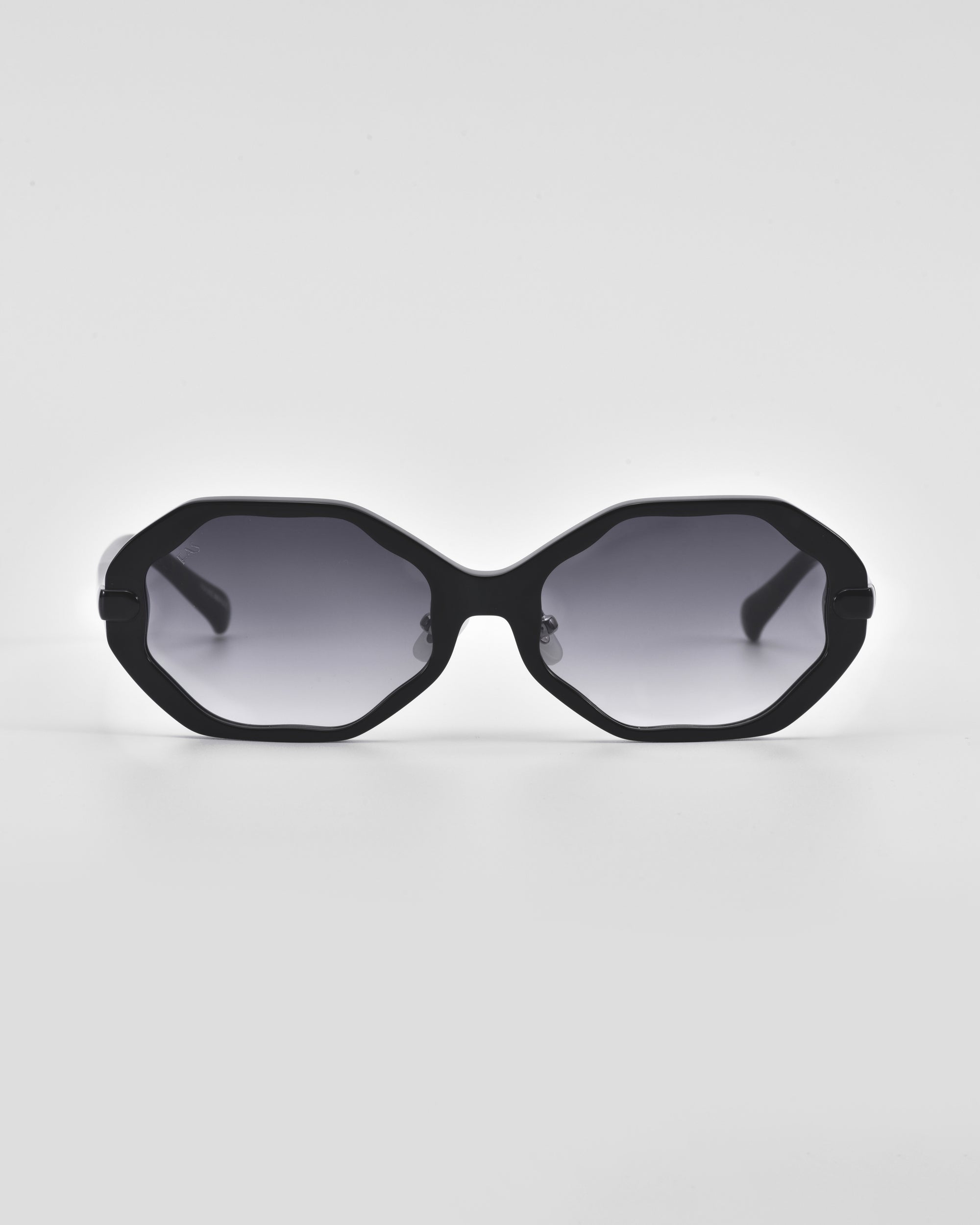 A pair of black octagonal Lotus sunglasses by For Art&#39;s Sake® with gray-tinted lenses set against a white background. The design is minimalist, featuring thin temples and no visible branding or adornments. Jade-stone nose pads and the clean, angular silhouette give these sunglasses a modern and stylish appearance.
