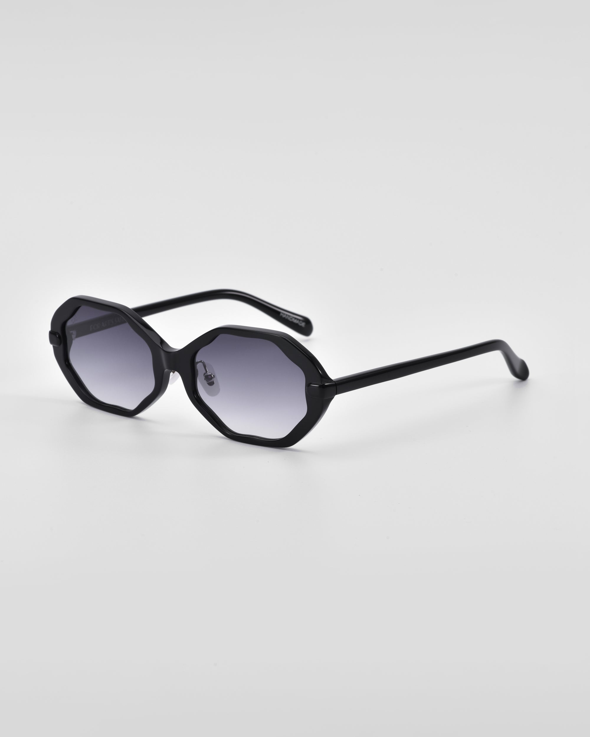 A pair of black octagonal sunglasses with dark tinted lenses is displayed against a plain white background. The For Art's Sake® Lotus sunglasses feature a modern geometric design, sleek temples, and jade-stone nose pads for added elegance.