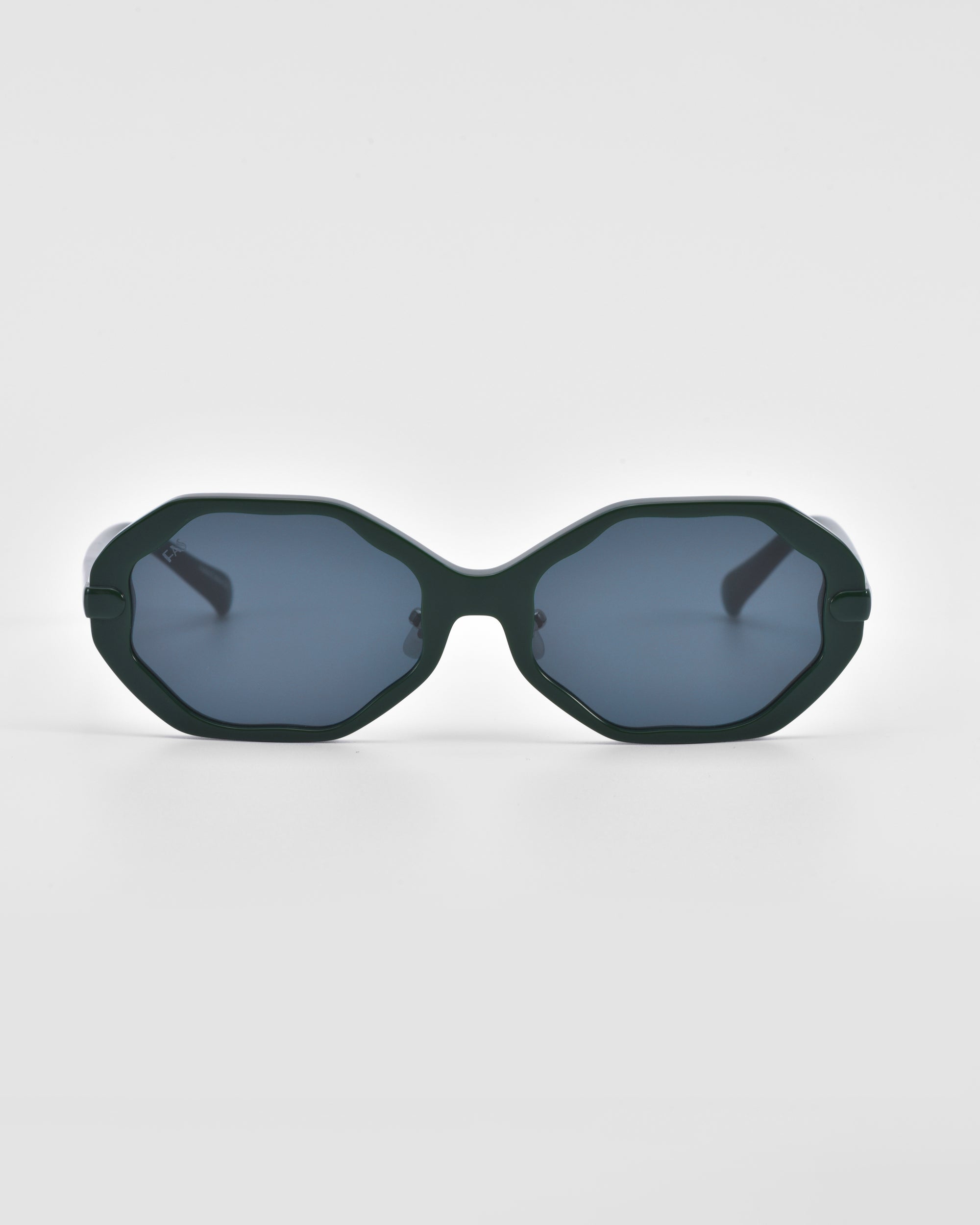 A pair of octagonal, dark green For Art&#39;s Sake® Lotus sunglasses with grey-tinted lenses is centered on a white background. The angular silhouette features a thick frame and jade-stone nose pads, offering a modern geometric design that creates a distinctive, stylish look.