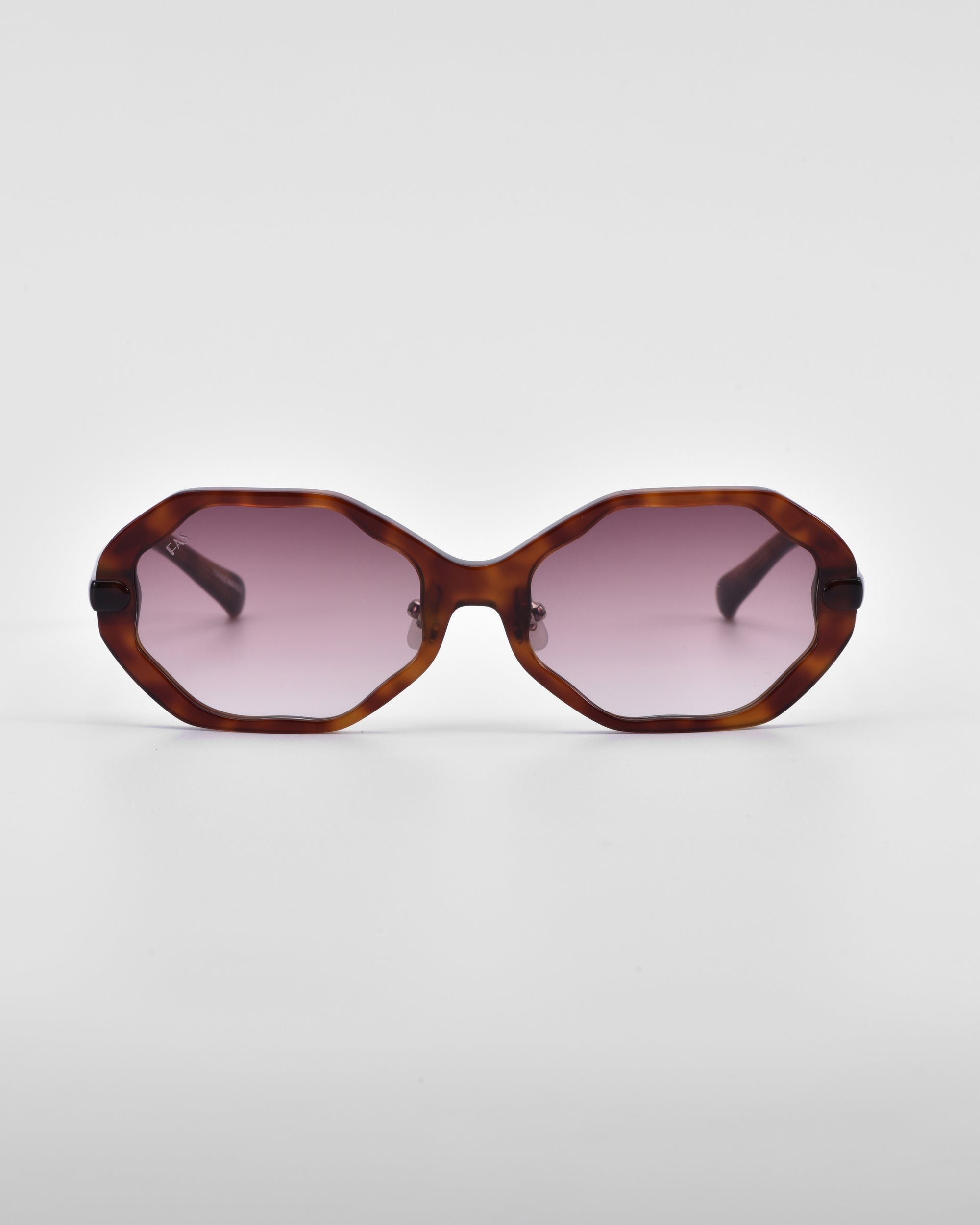 Front view of a pair of Lotus sunglasses by For Art's Sake® with an angular silhouette, featuring tortoiseshell frames and pink-tinted lenses, complemented by jade-stone nose pads. The sunglasses are placed on a plain white background.