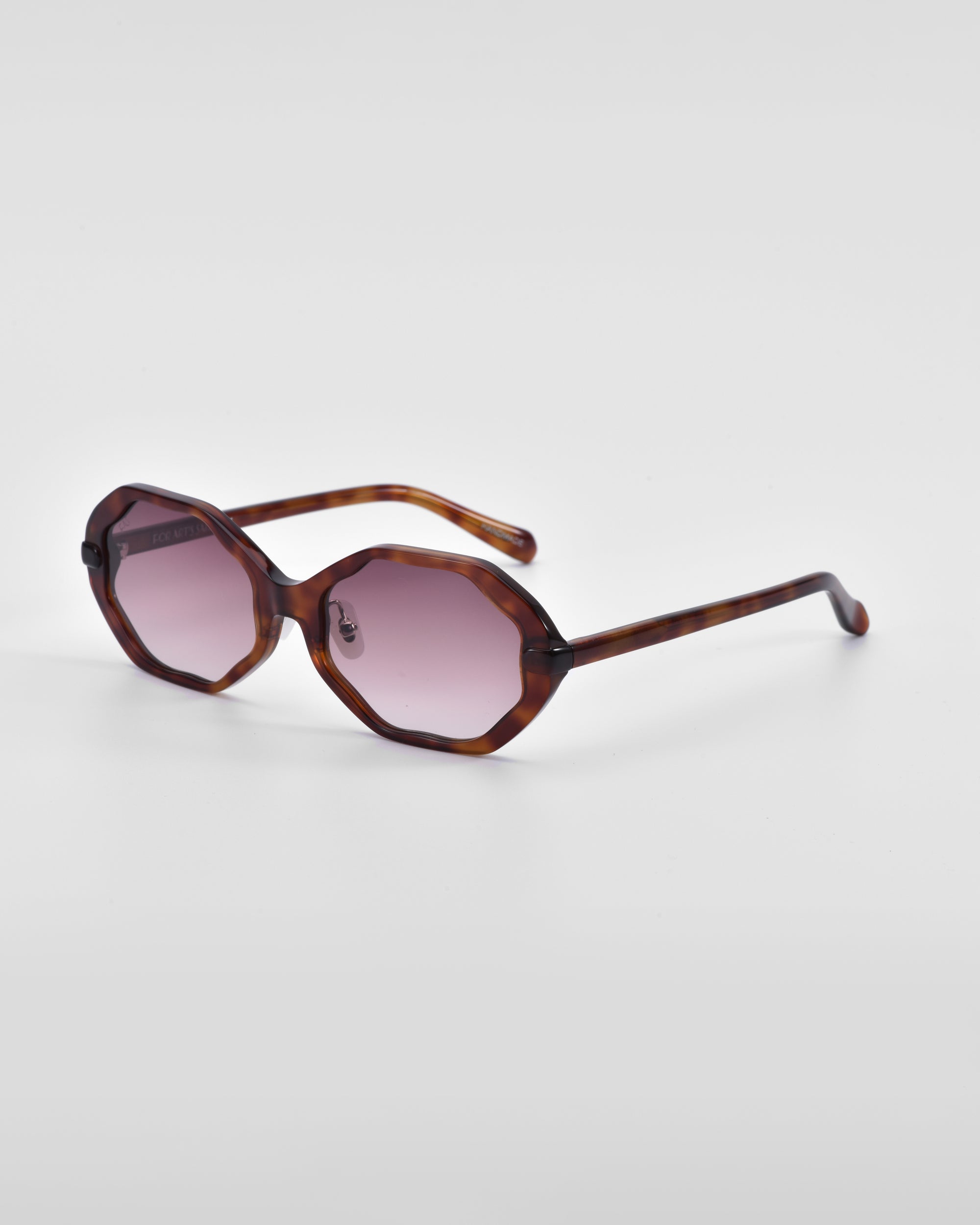 A pair of For Art&#39;s Sake® Lotus sunglasses with tortoiseshell frames and round pink-tinted lenses is placed against a white background. The frame, featuring an angular silhouette, has a distinct, slightly geometric design and slender arms.