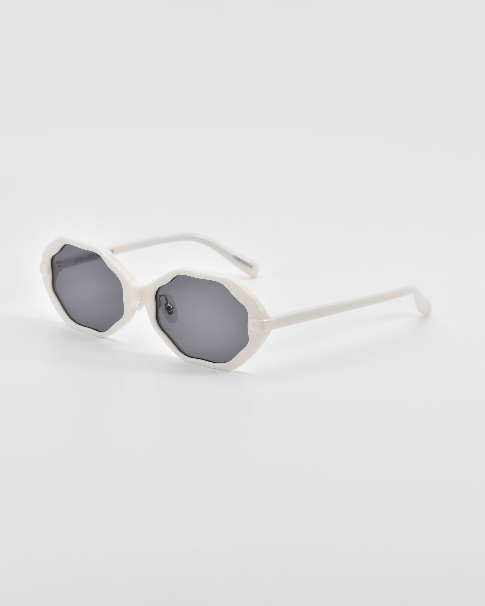 A pair of For Art&#39;s Sake® Lotus sunglasses with white, scalloped-edge frames and dark tinted lenses. They have thin, straight arms and jade-stone nose pads, positioned against a plain, light gray background.