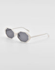 A pair of For Art's Sake® Lotus sunglasses with white, scalloped-edge frames and dark tinted lenses. They have thin, straight arms and jade-stone nose pads, positioned against a plain, light gray background.