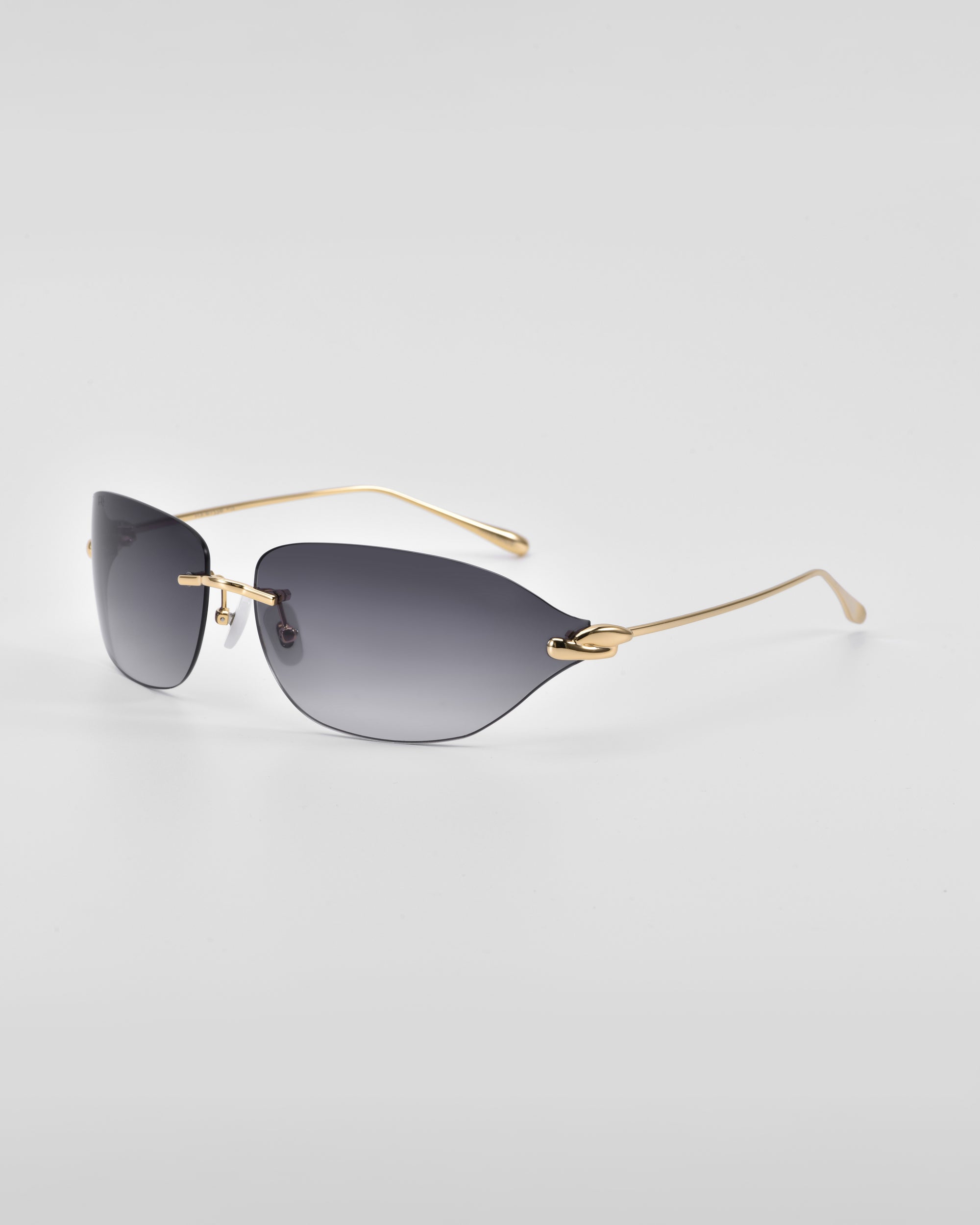 A pair of stylish For Art&#39;s Sake® Serpent I rimless sunglasses with dark tinted lenses and golden thin arms, photographed on a white surface. The minimalistic design, featuring 18-karat gold plating, gives them a sleek, modern look.