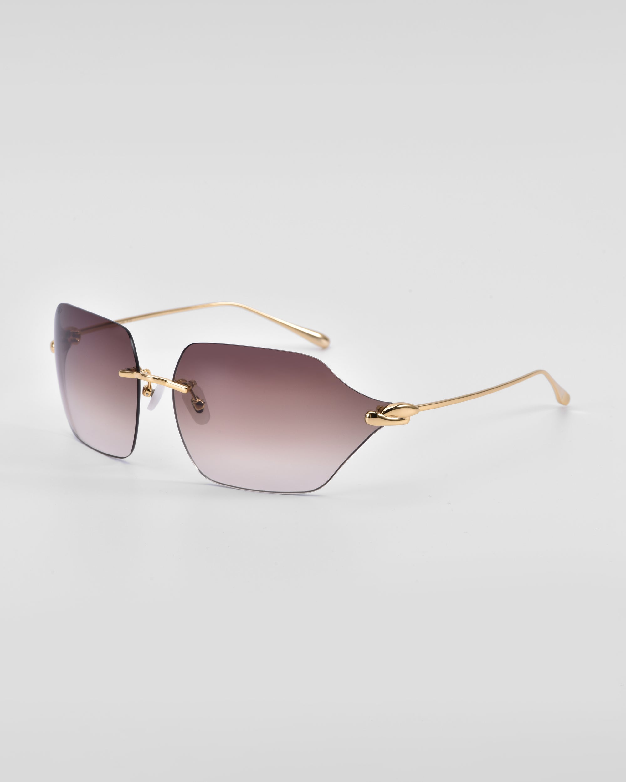 A pair of fashionable For Art&#39;s Sake® Serpent II sunglasses with gradient lenses from dark to light gray, featuring a frameless wrap lens design and thin, metallic 18-karat gold-plated temples and bridge. The temples have a slight curve, and the overall design is sleek and modern.