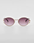 A pair of stylish For Art's Sake® 'Sky' sunglasses with gold frames and dark purple gradient lenses. The temple arms are intricately designed, adding an elegant touch to the overall look. Natural jade-stone nose pads offer added comfort, and the background is plain white, highlighting the sunglasses beautifully.