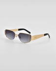 A pair of stylish sunglasses boasting 18-karat gold frames and dark gradient lenses. The temples are wide with a gold finish, transitioning to black at the ends. The plain white background accentuates the luxurious and contemporary design of these For Art's Sake® Talia metal-framed sunglasses.