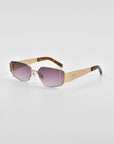 A pair of For Art's Sake® Talia designer sunglasses with 18-karat gold metallic frames and gradient purple-tinted lenses. The arms of the sunglasses are gold with tortoiseshell patterning near the ends. The sunglasses are set against a plain white background.