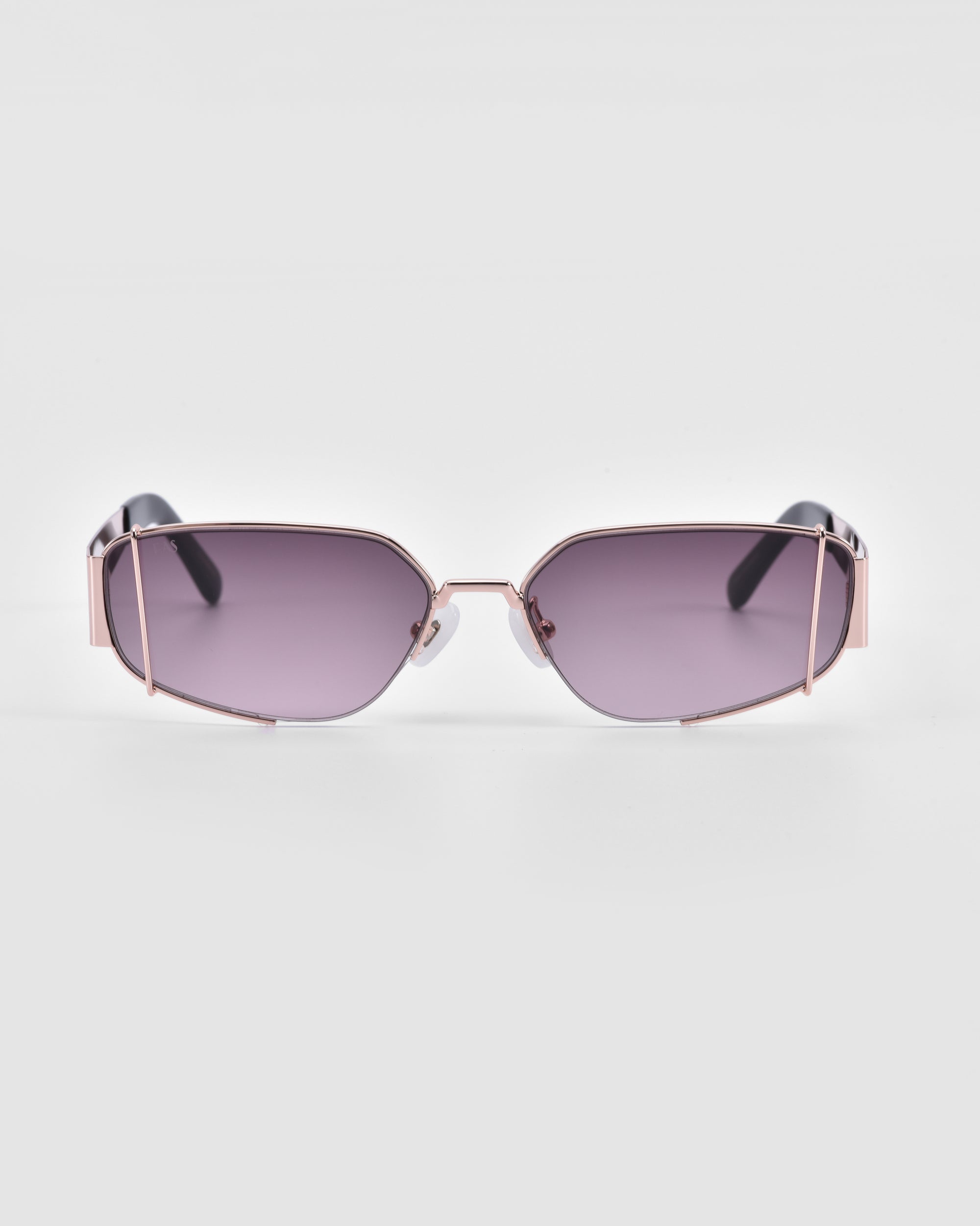 A pair of stylish Talia sunglasses from For Art&#39;s Sake® with hexagonal, purple-tinted lenses and 18-karat rose gold metal frames. The temples have black tips, and the lenses feature a sleek, minimalist design. The background is plain white.