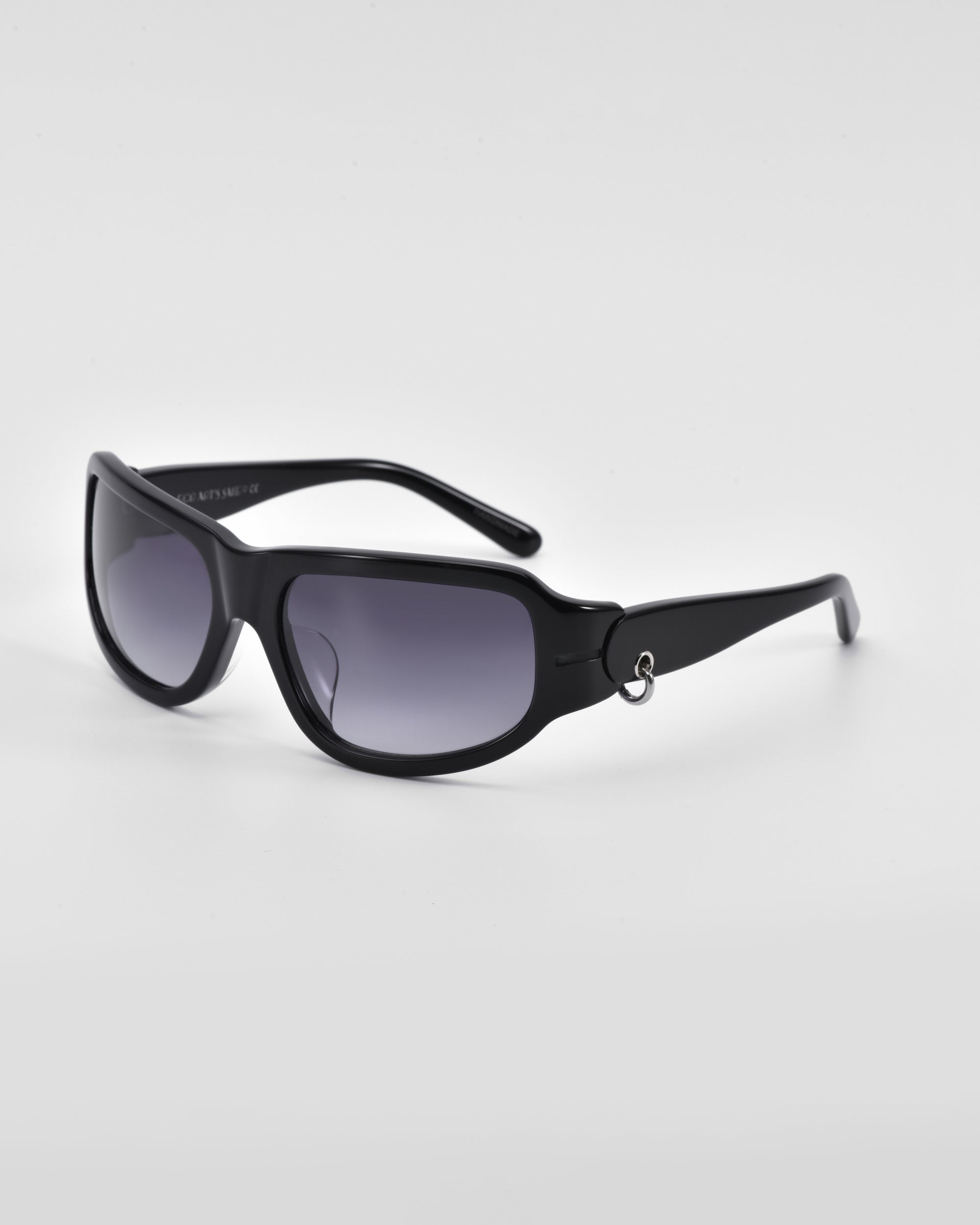 A pair of sleek For Art&#39;s Sake® Raven sunglasses with dark tinted lenses set against a plain white background. The sunglasses feature a simple, modern design with slightly curved arms and a small metallic 18-karat gold detail near the hinges.