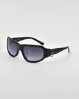 A pair of sleek For Art's Sake® Raven sunglasses with dark tinted lenses set against a plain white background. The sunglasses feature a simple, modern design with slightly curved arms and a small metallic 18-karat gold detail near the hinges.