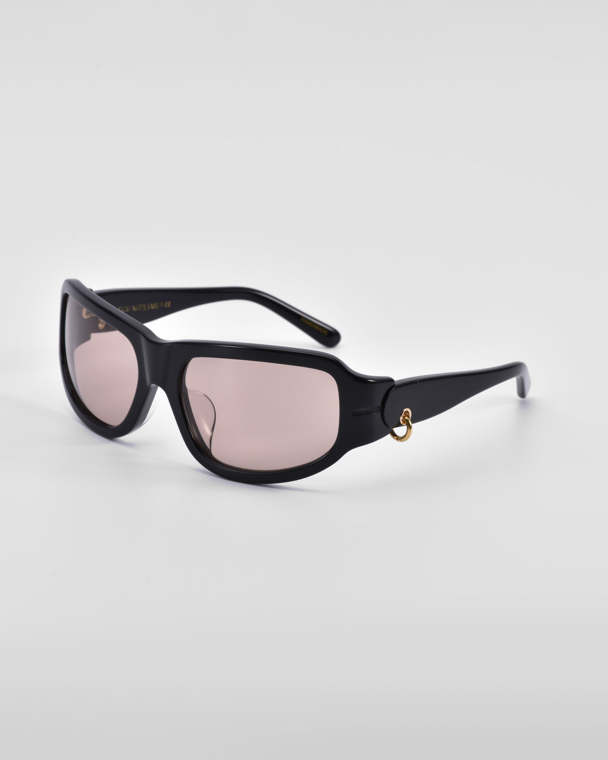 A pair of sleek black For Art&#39;s Sake® Raven sunglasses with slightly tinted lenses is displayed against a plain white background. The sunglasses feature a small 18-karat gold ring on each temple, adding a subtle touch of elegance.