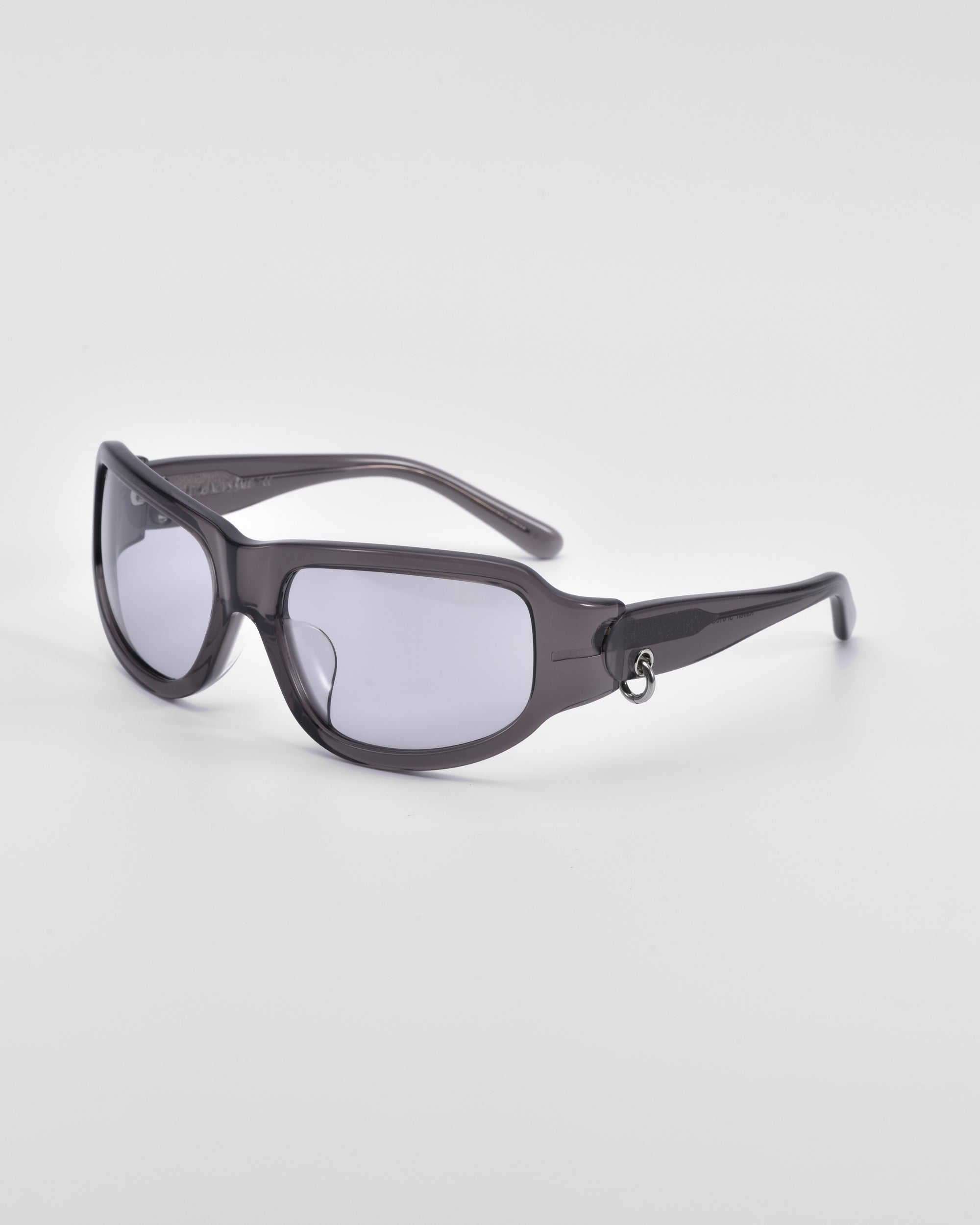 A pair of sleek, dark-colored For Art&#39;s Sake® Raven sunglasses with a small decorative metal ring on the temple arm. The lenses are tinted grey, and the frames are curved for a snug fit. Perfectly embodying the stylish flair of Y2K wrap sunglasses, they stand out against a plain white background.