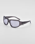 A pair of sleek, dark-colored For Art's Sake® Raven sunglasses with a small decorative metal ring on the temple arm. The lenses are tinted grey, and the frames are curved for a snug fit. Perfectly embodying the stylish flair of Y2K wrap sunglasses, they stand out against a plain white background.