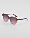 A pair of oversized cat-eye sunglasses with gradient lenses that transition from dark to light pink. The frame is a sleek, dark brown with 18-karat gold plating near the hinges. The design is chic and modern, making it a true statement piece suitable for both casual and formal wear. Introducing "Helene" by For Art's Sake®.