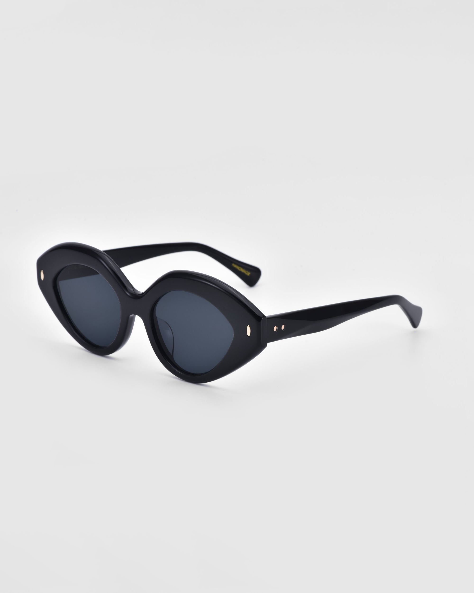 A pair of Vera sunglasses from For Art's Sake®, featuring black, oval-shaped frames with dark lenses and thick edges. The eco-friendly eyewear is positioned at an angle on a plain white background, showcasing both the front and side views.